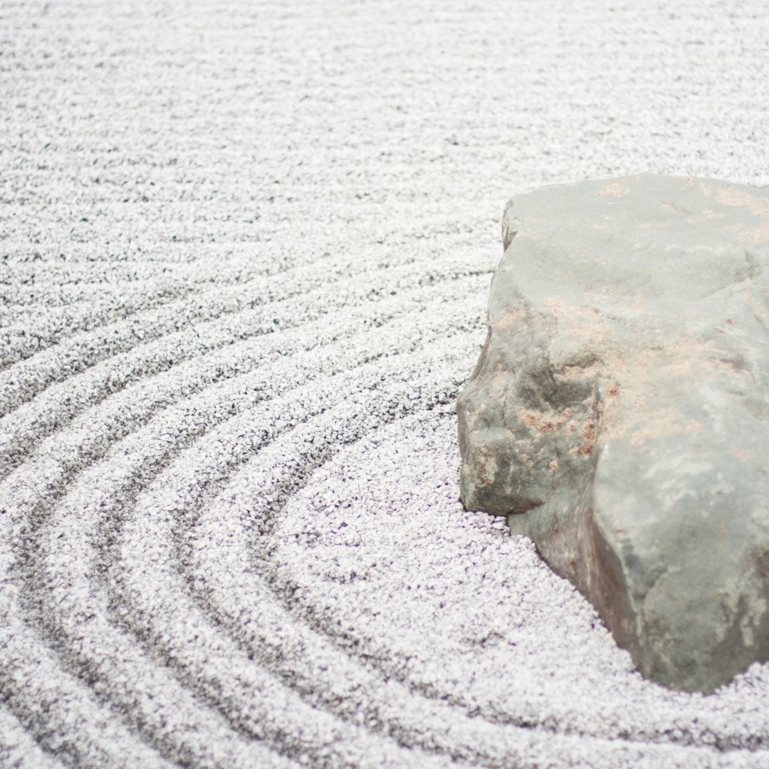 Un gros rocher trône au milieu d'un jardin zen minimaliste, entouré de gravier blanc soigneusement ratissé formant des cercles concentriques autour de la pierre.