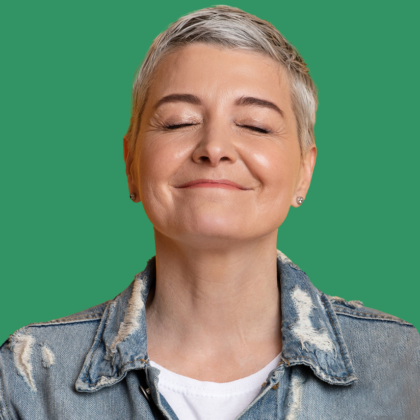 A person with short gray hair and closed eyes smiles softly against a green background. 